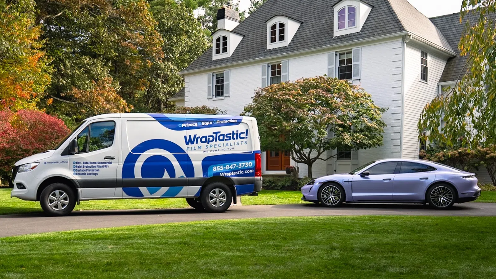 Wraptastic service van and luxury car parked in front of large white house with autumn trees.
