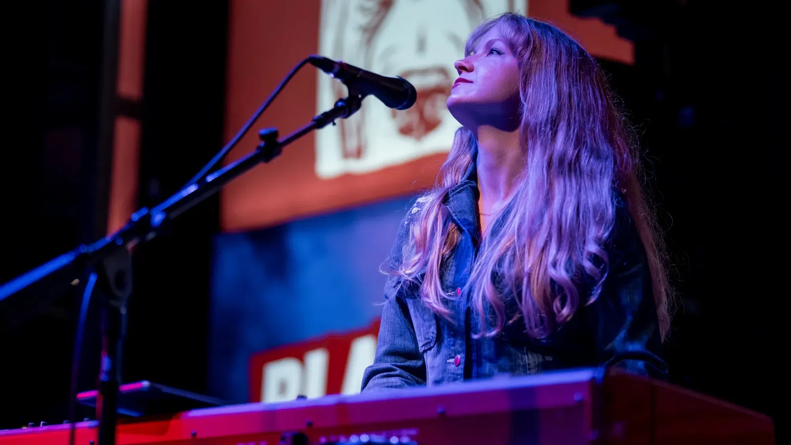 Female musician playing keyboard and singing into microphone on stage with colorful lighting