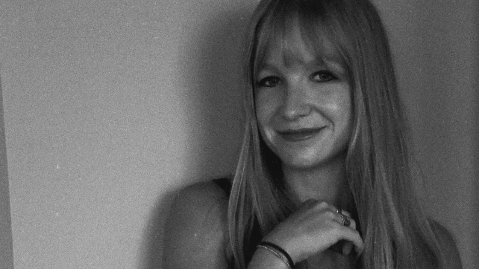 Black and white portrait of a smiling woman with long hair and a tattoo on her forearm that reads beauty for ashes.