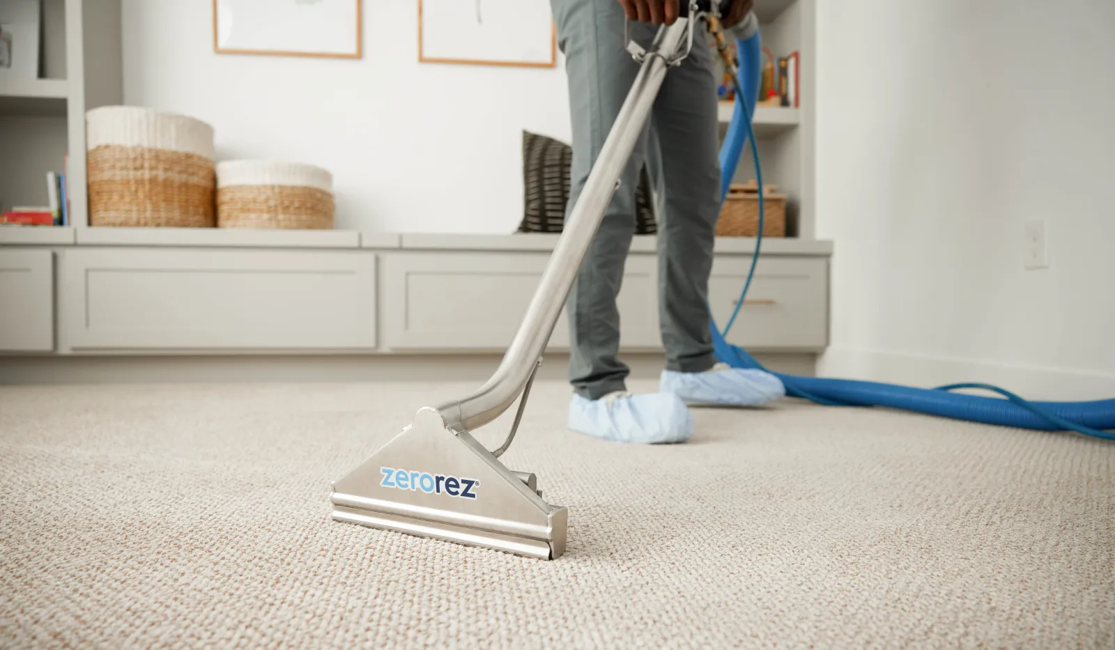Professional carpet cleaning with ZeroRez equipment in a clean, modern living room with gray cabinetry and wicker baskets.