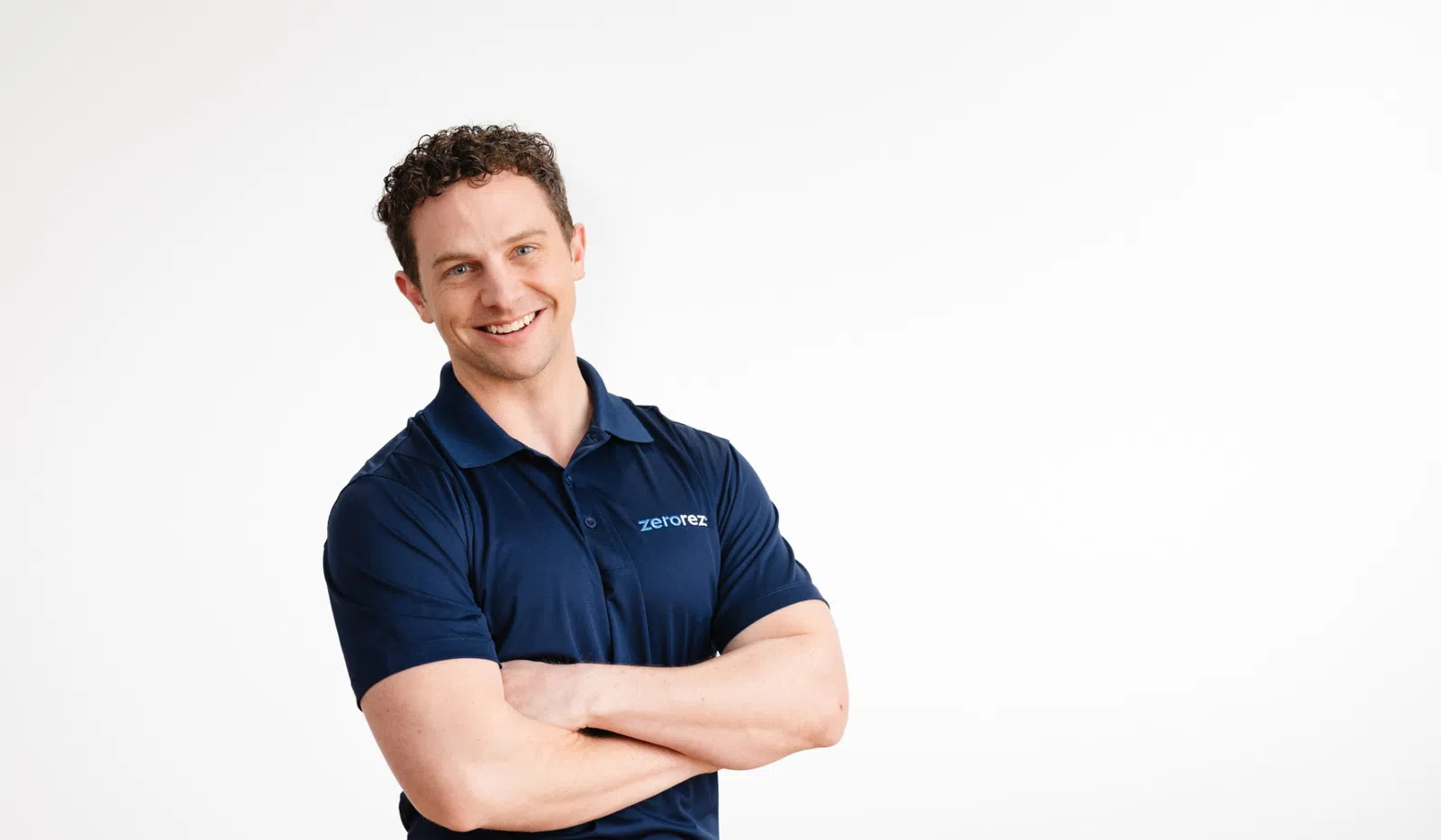 Smiling man in navy blue Zerorez polo shirt stands with arms crossed against a white background.