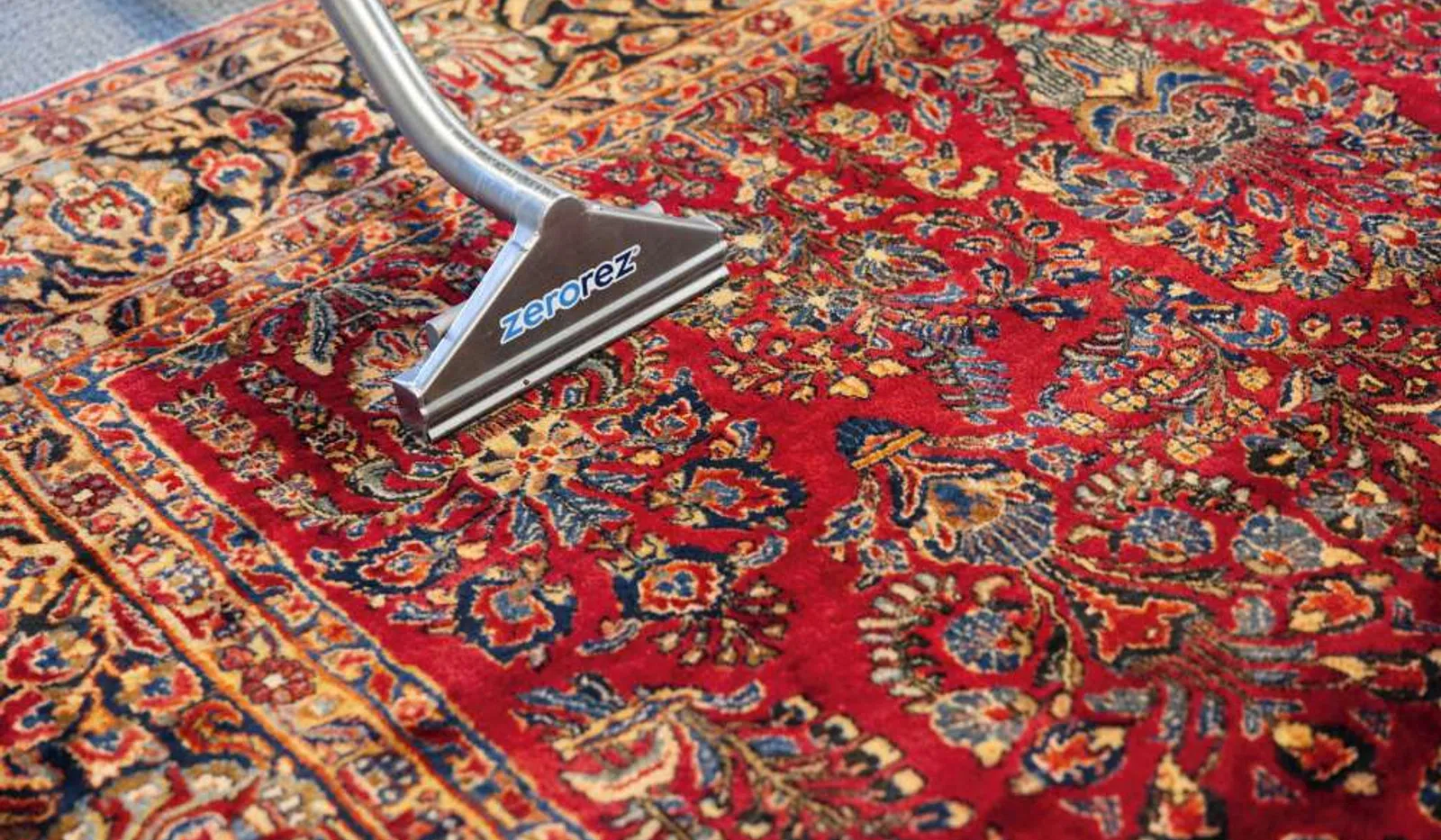 Carpet cleaning tool deep cleans vibrant red and blue patterned oriental rug with detailed floral designs.