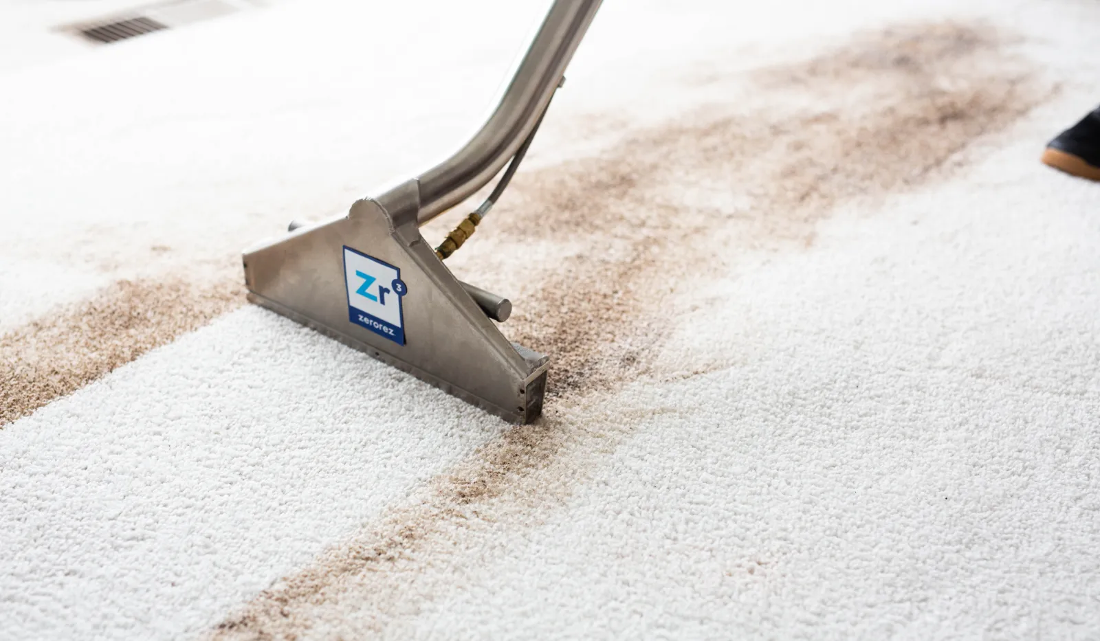Carpet cleaning machine removing dirt from white carpet, showing clear contrast between cleaned and dirty areas.