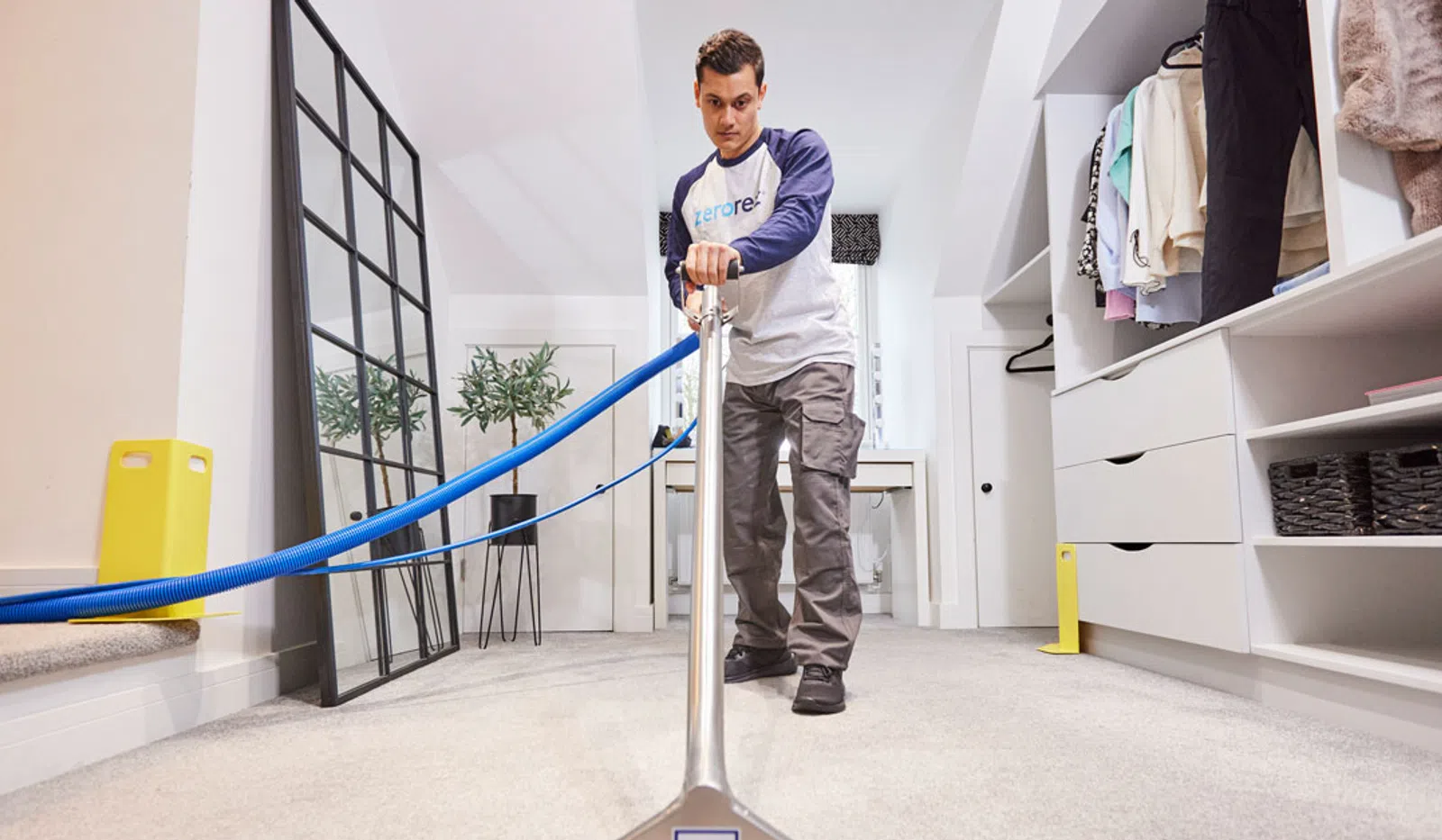 Professional cleaner using carpet cleaning machine in a modern home closet with clothes and drawers