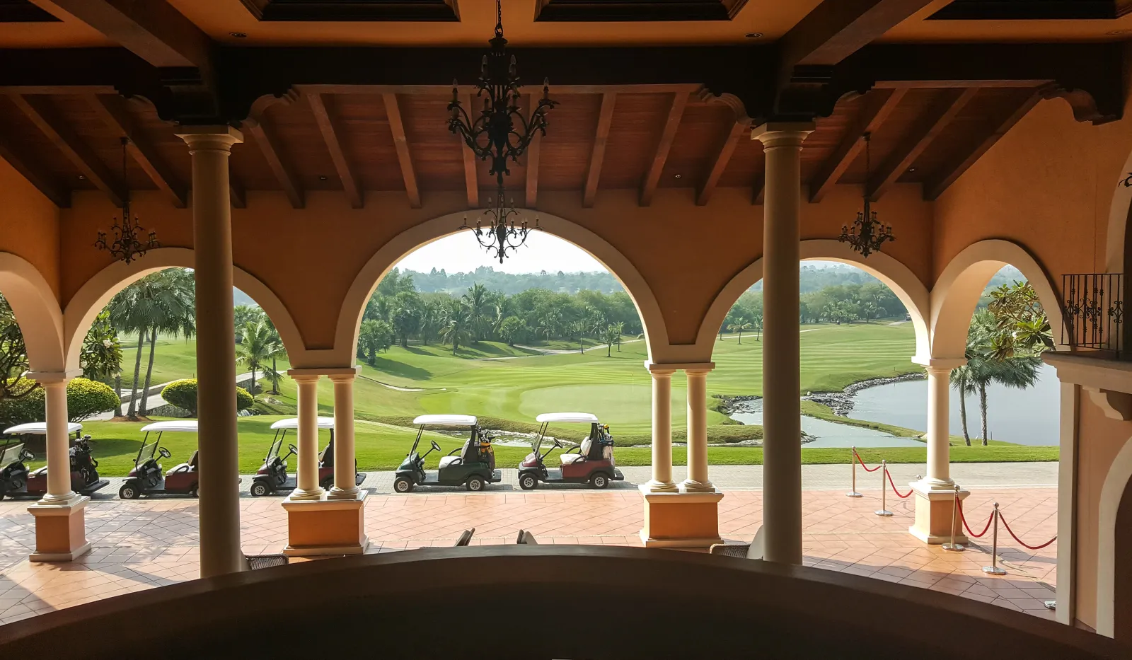 View of golf course with golf carts lined up under arched terrace with columns and chandeliers.