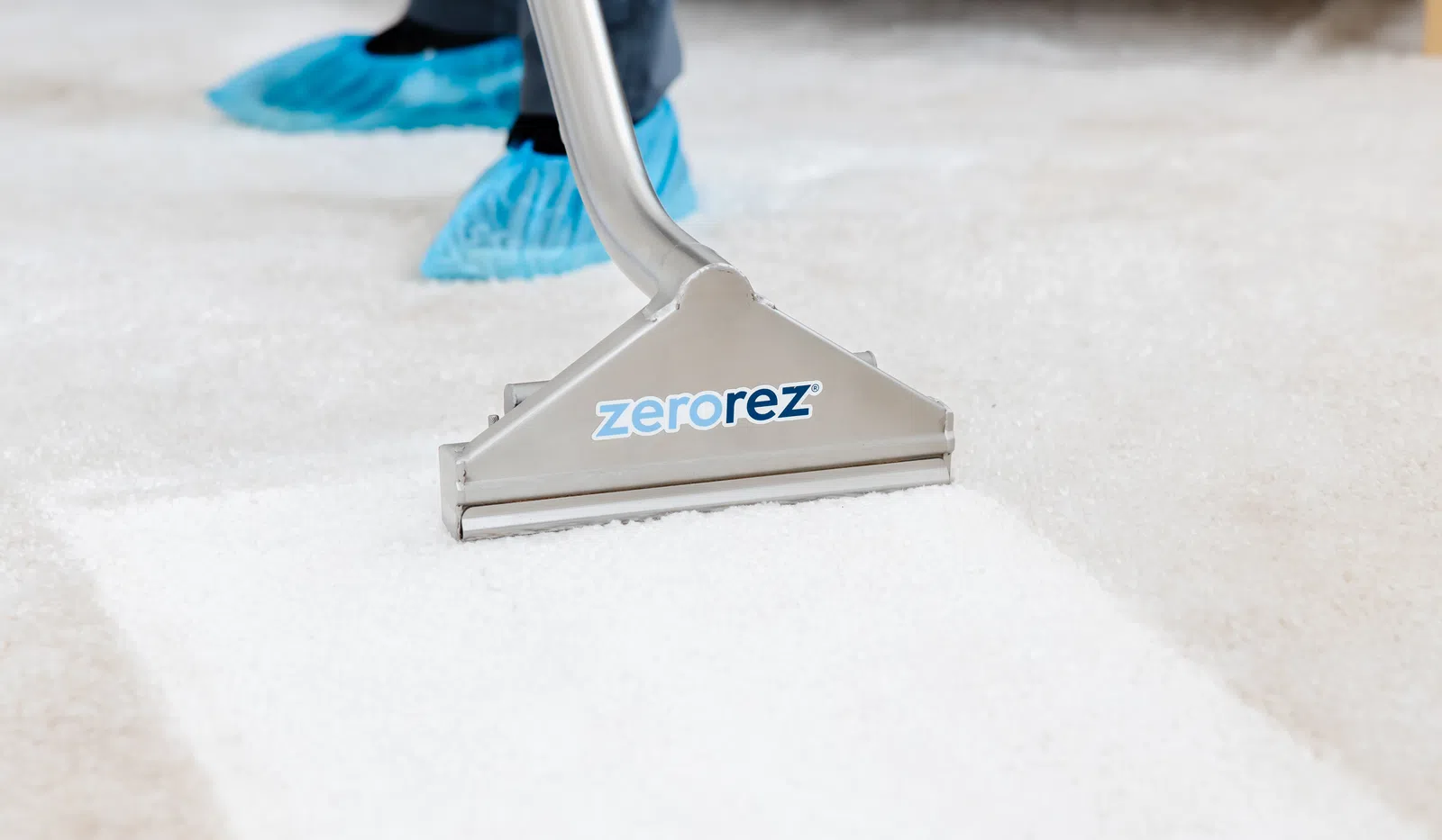 Carpet cleaning machine removing dirt from white carpet with visible clean area and protective shoe covers.
