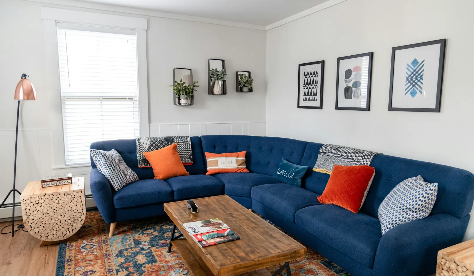 Modern living room with blue sectional sofa, wooden coffee table, colorful cushions, patterned rug, and wall art.