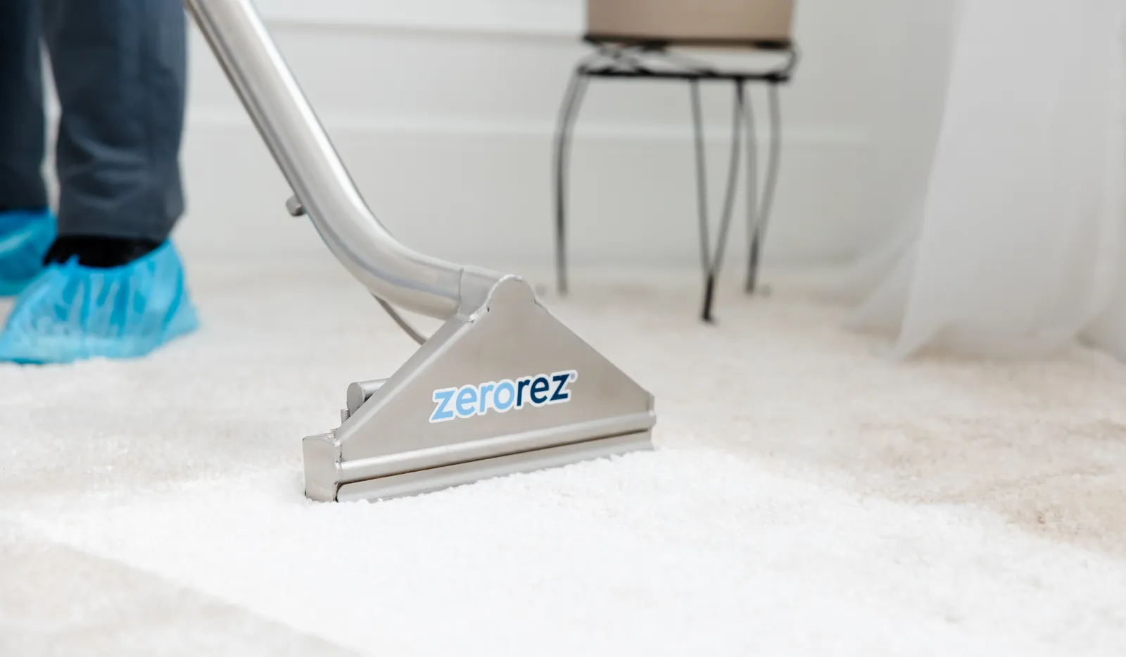 Professional carpet cleaning with Zerorez equipment on white carpet by technician wearing blue shoe covers.