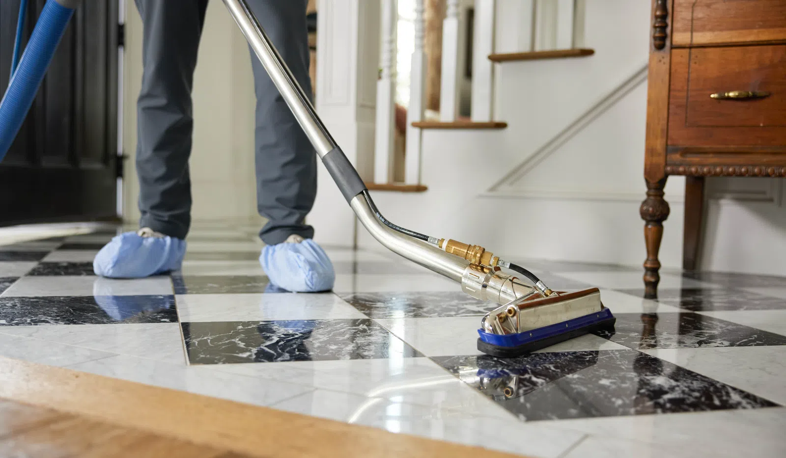 A cleaner using a professional carpet cleaner on a polished black and white tile floor in a stylish home.