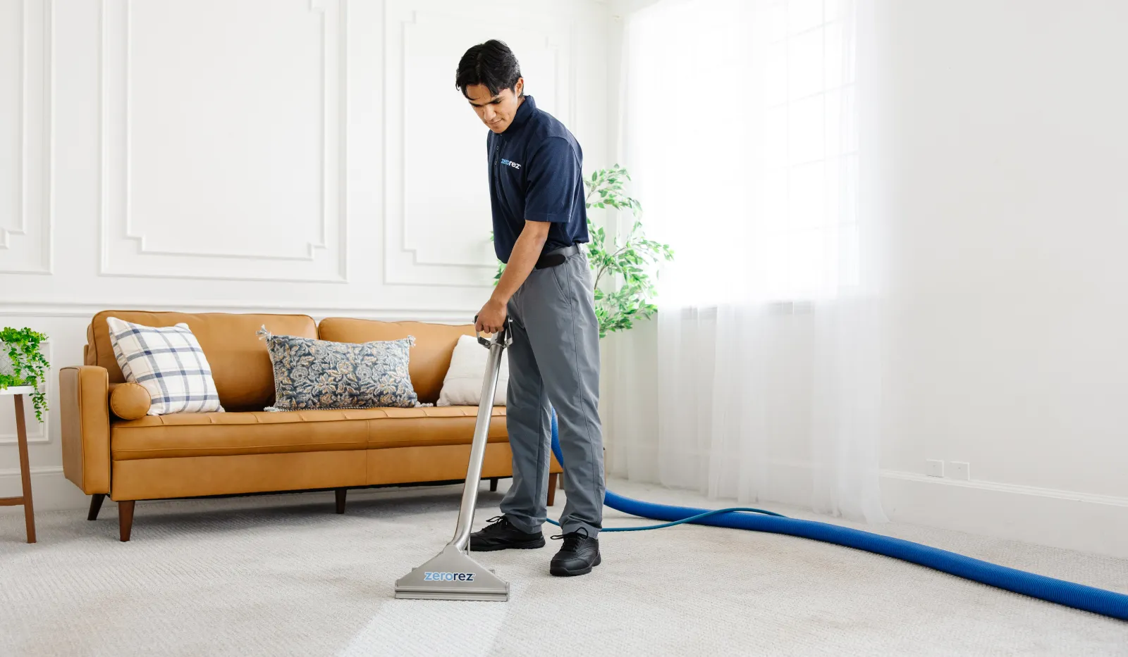 Professional carpet cleaner using a specialized machine to clean a white carpet in a bright living room.