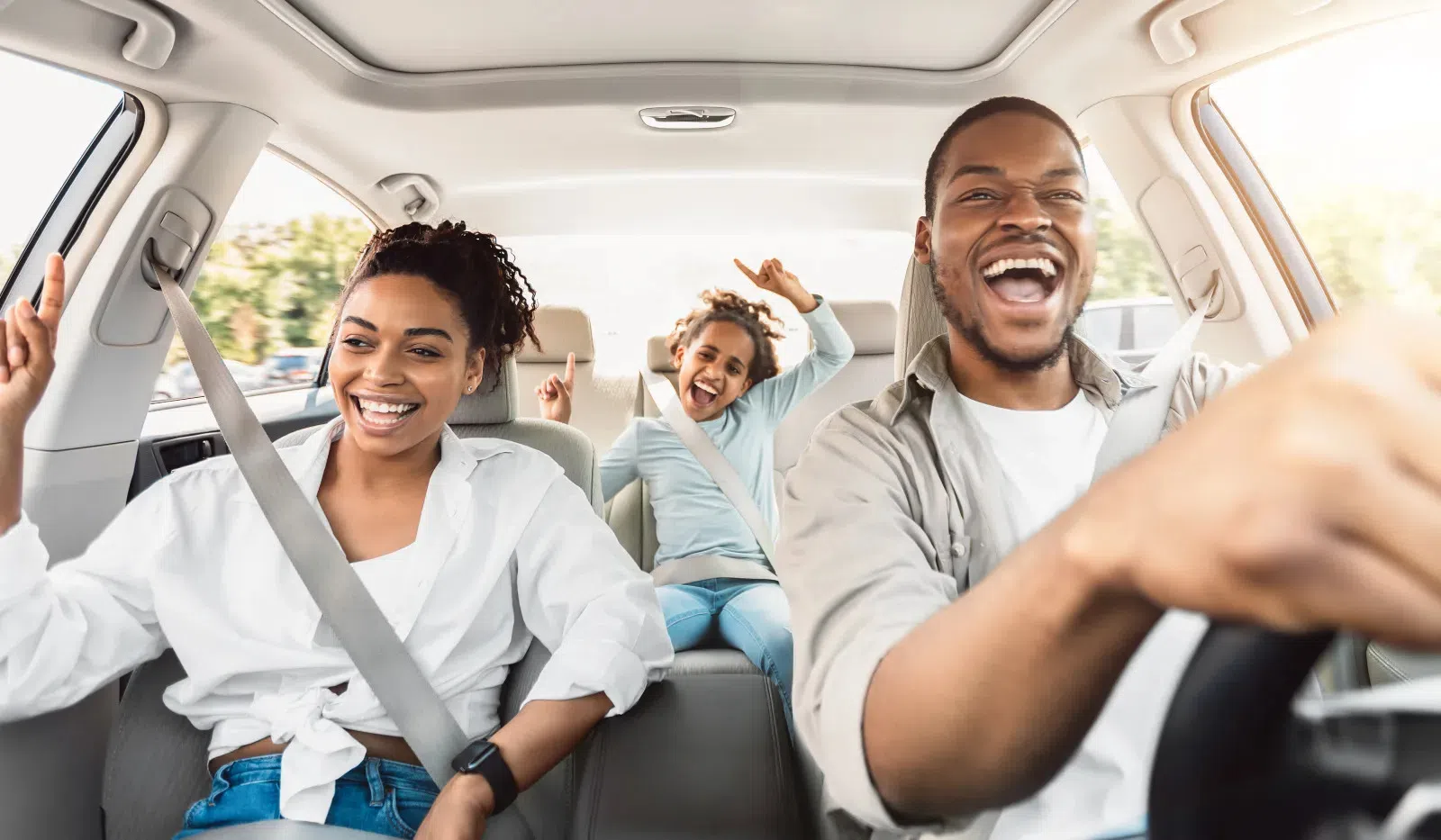 Happy family of three enjoying a car ride with smiles and raised hands inside a modern vehicle
