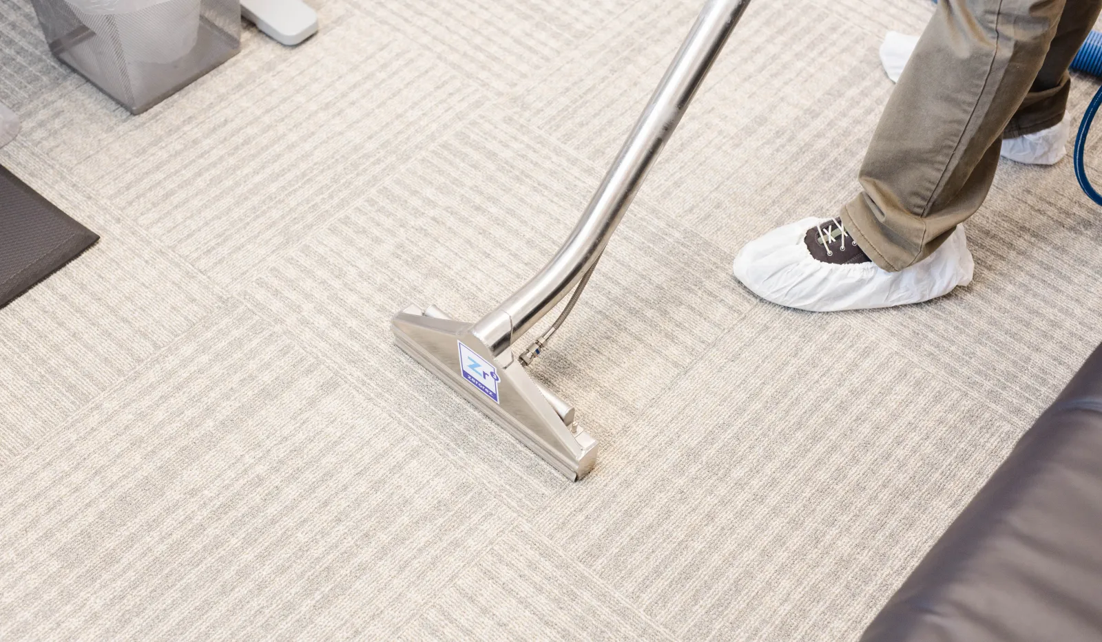 Professional cleaning of light-colored office carpet using a carpet cleaning machine and shoe covers.