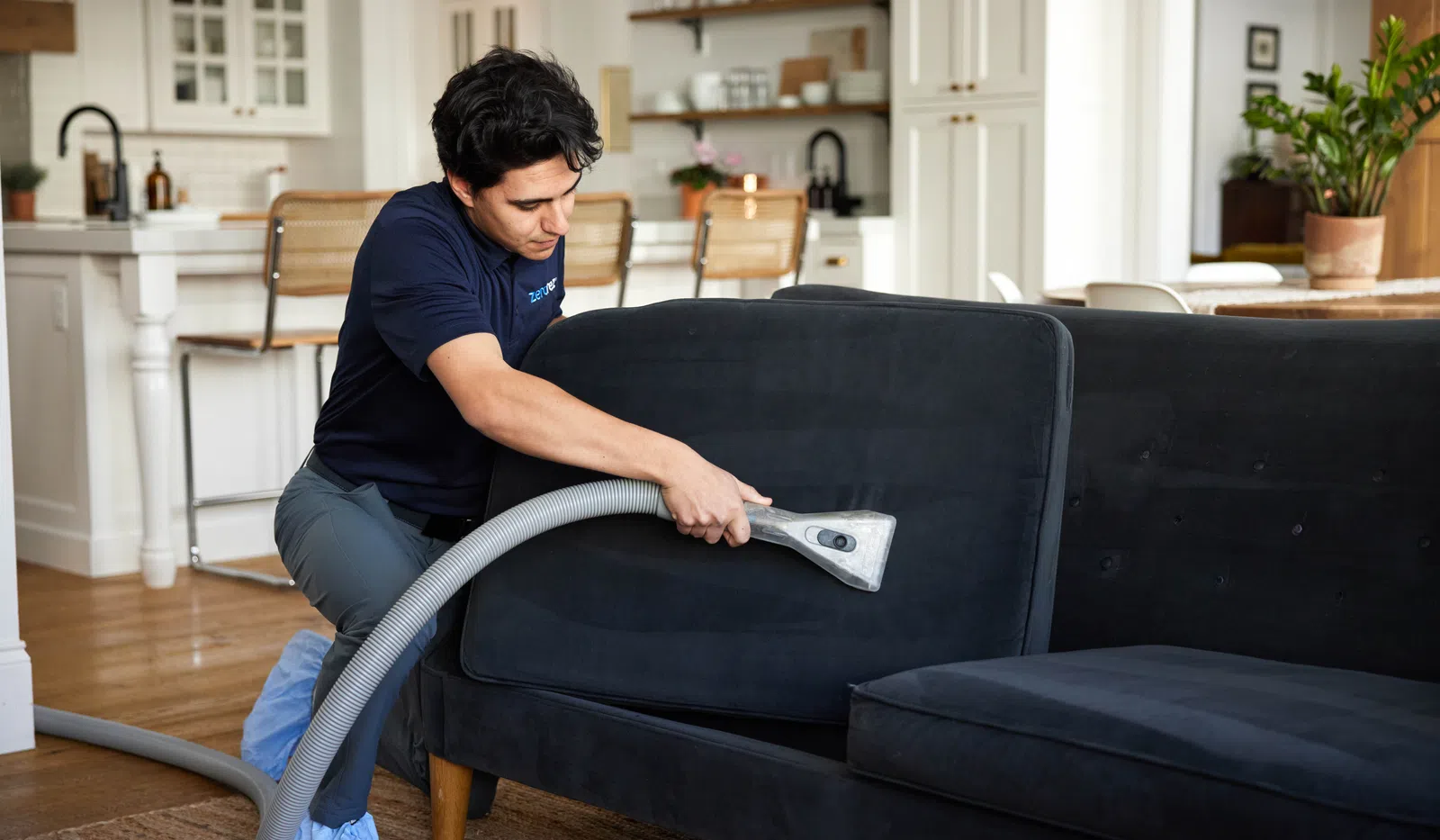 A professional cleaning service vacuums a couch in a modern living room, ensuring a spotless home environment.