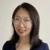 Portrait of smiling woman with glasses and dark hair wearing a navy blue top against a plain background