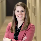 Confident woman in a pink blazer and black polka dot shirt standing with arms crossed indoors