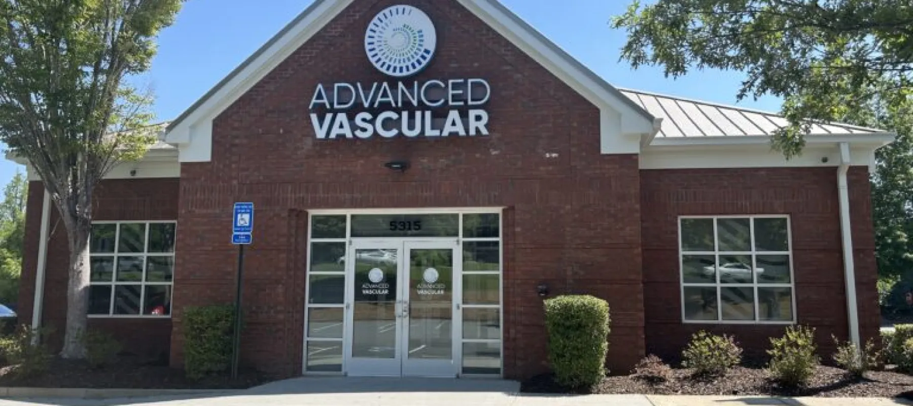 Front view of Advanced Vascular medical office building with brick facade and parking area in daylight.