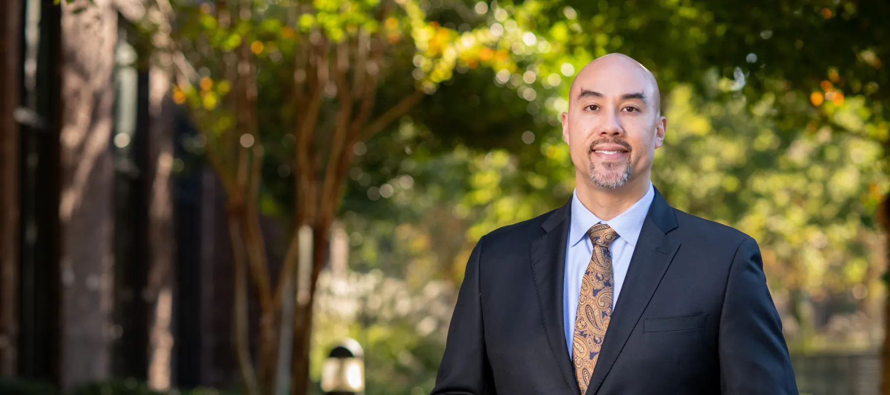 Confident male doctor in white coat with paisley tie and watch against a neutral gray background