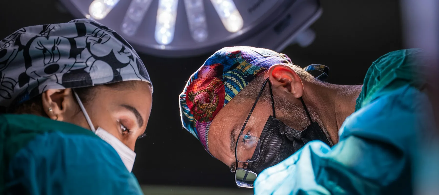 Surgeons wearing masks and scrubs performing surgery under bright operating room light.