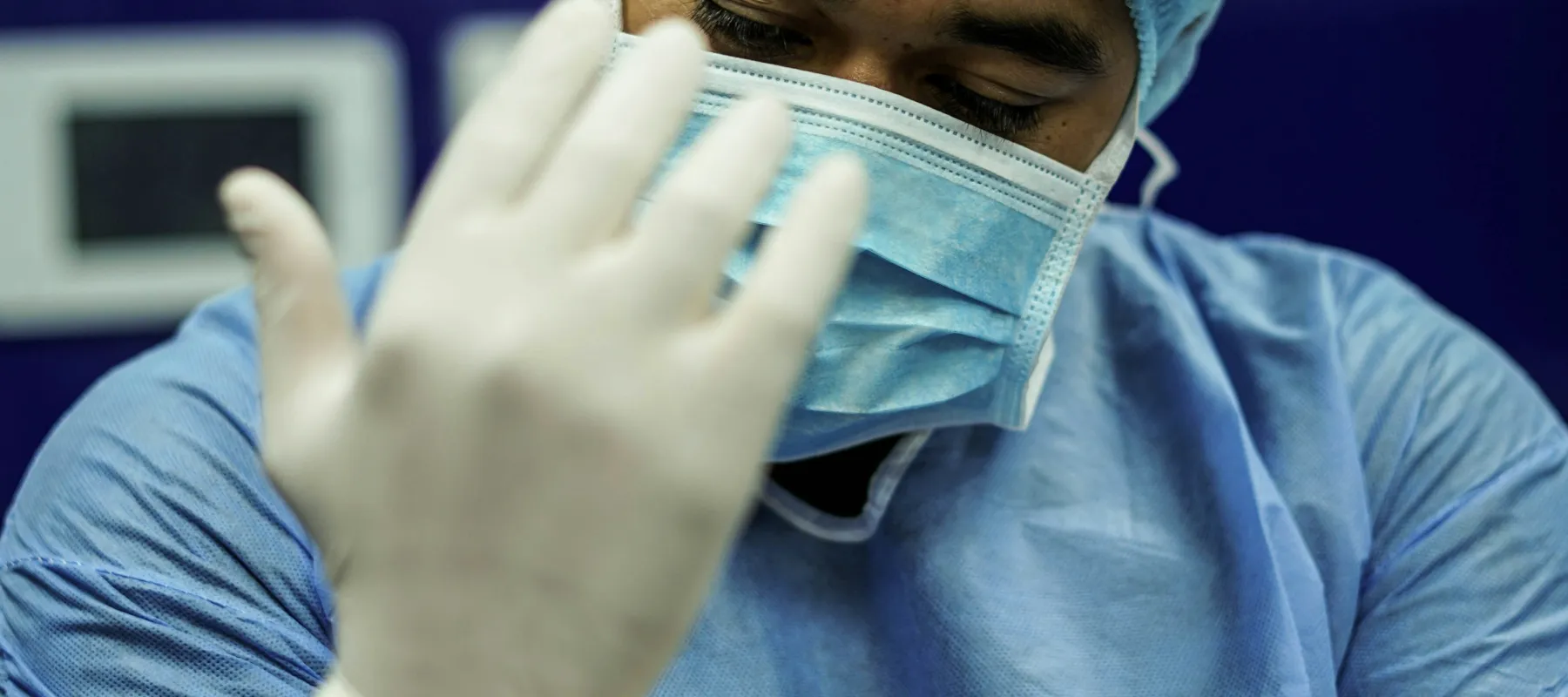 Healthcare worker wearing protective gear and gloves preparing for a medical procedure in a clinical setting.