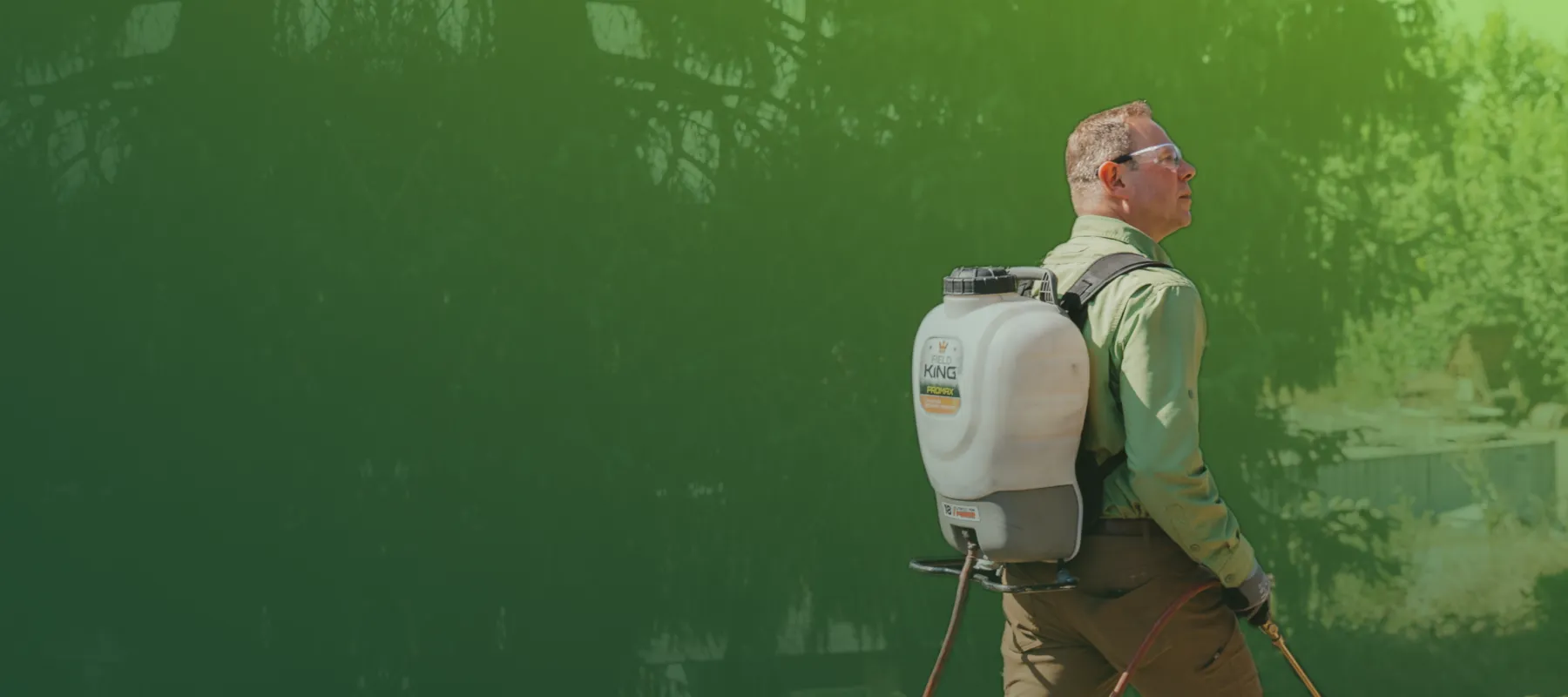 Man wearing protective gear with a backpack sprayer applying chemicals outdoors in a garden or yard.