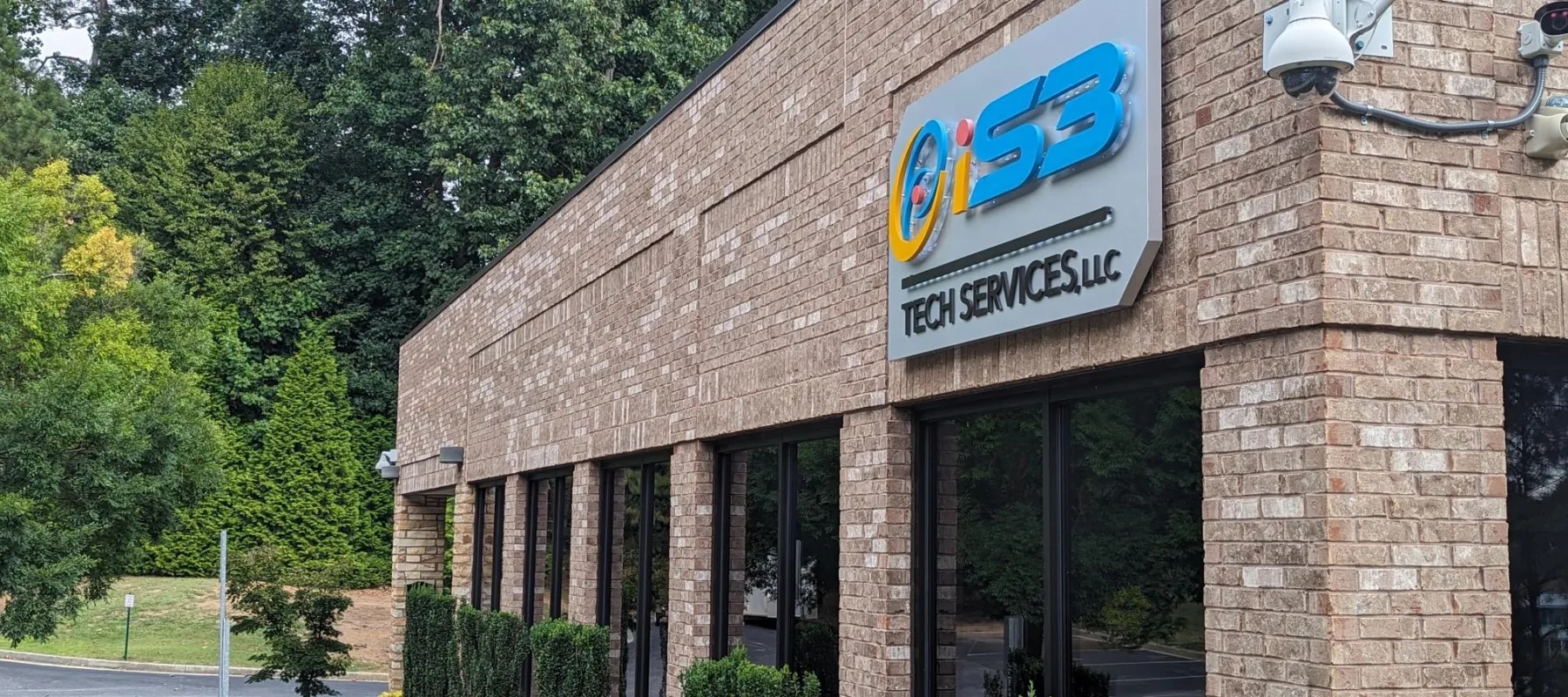 Brick office building with ISS Tech Services LLC sign and surrounding green trees and shrubs.