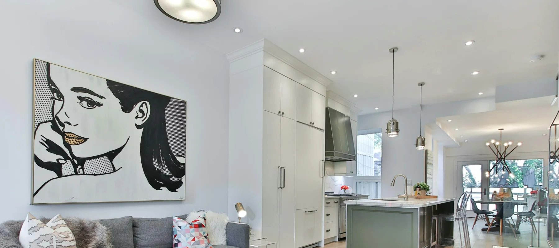Modern open living space with gray sofa, pop art wall, kitchen island, and light wood flooring in bright home.