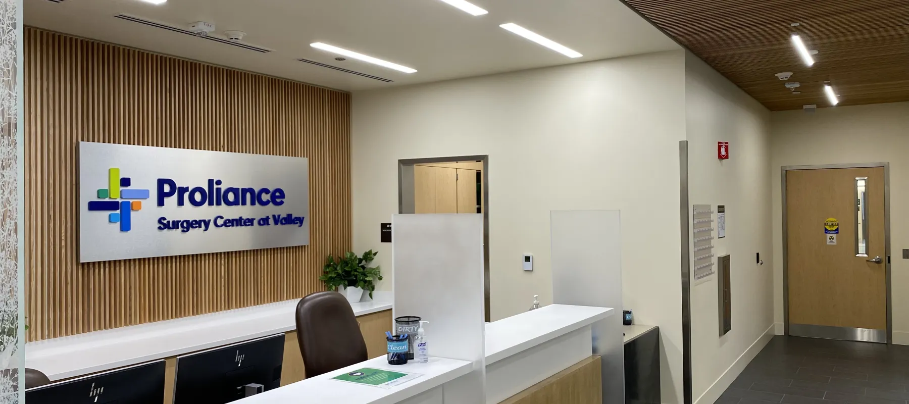 Reception area of Proliance Surgery Center at Valley with a white desk, computer monitors, and wooden accents.