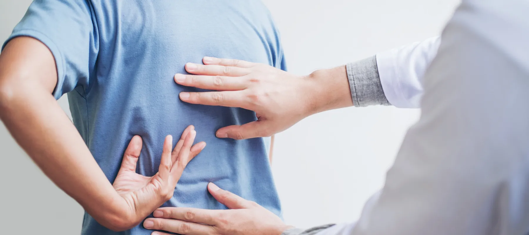 Doctor examining patient's lower back pain symptoms with hands during medical consultation.