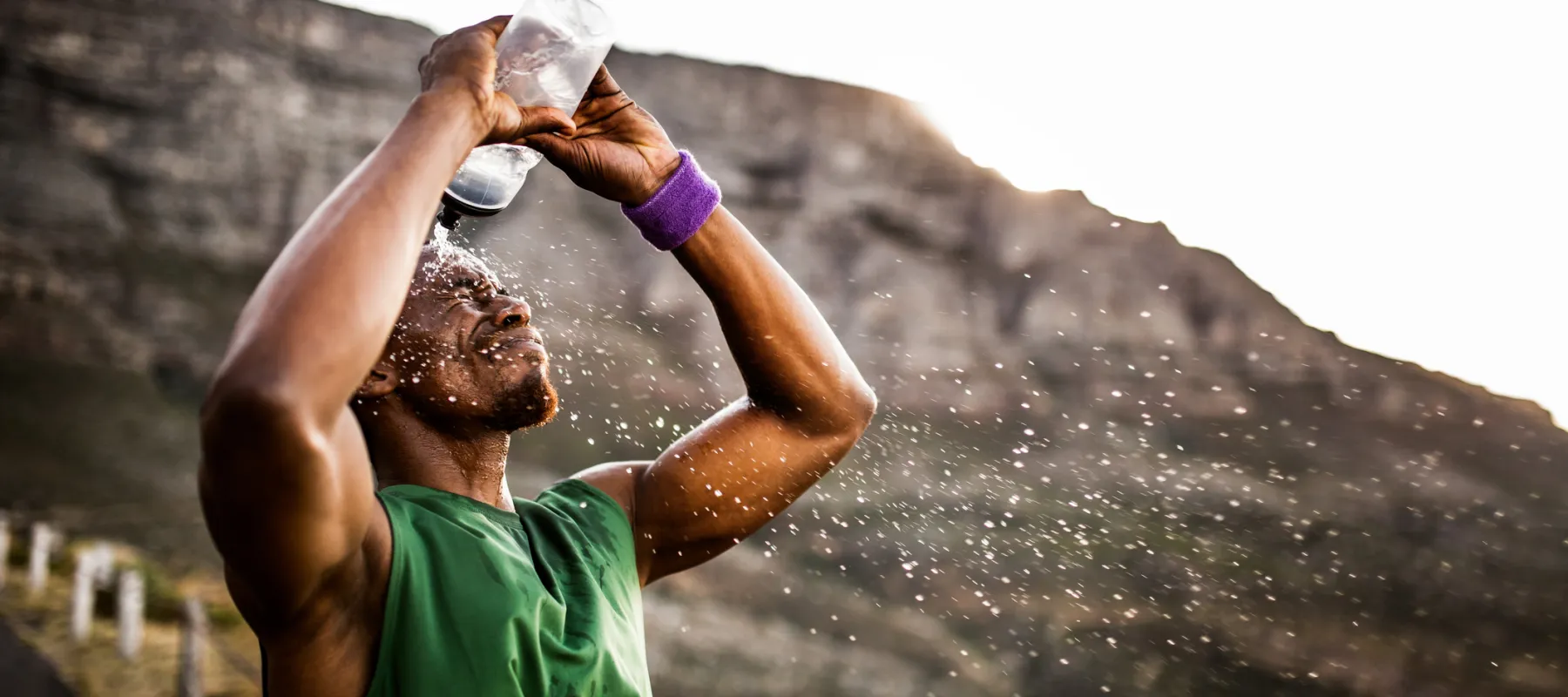 Athlete pouring water on his face outdoors with mountainous background during sunset or sunrise.