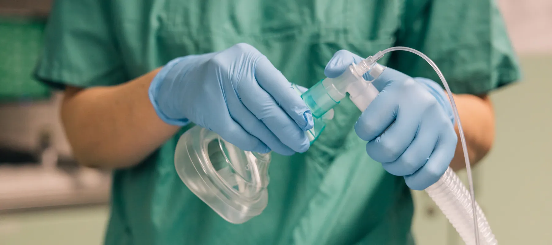 Healthcare professional in green scrubs adjusts oxygen mask tubing near patient in medical setting.