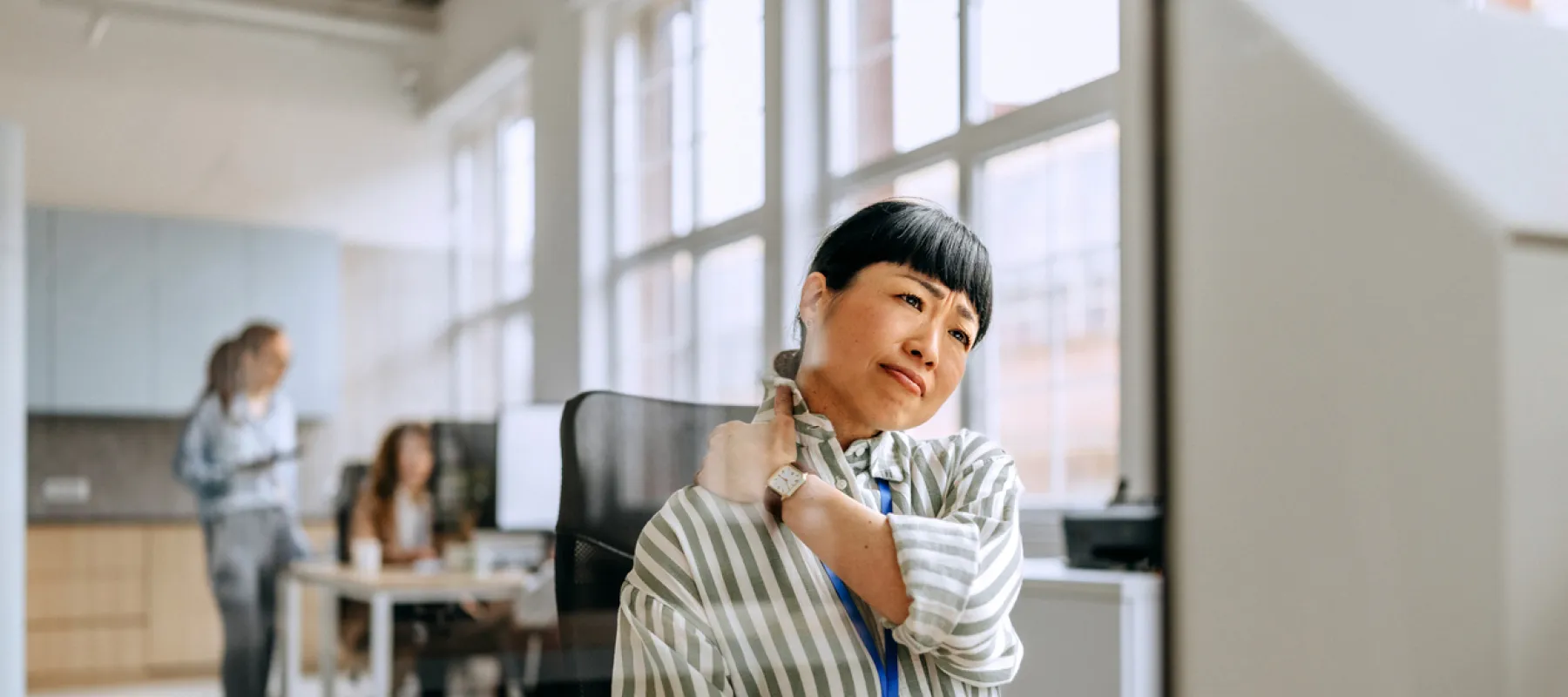 Woman sitting at office desk holding her neck in discomfort while looking at computer screen in modern workspace