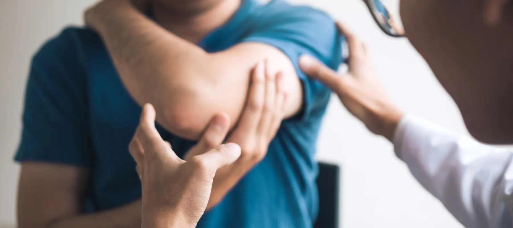Doctor examining a patient's elbow pain during a medical consultation in a clinical setting.