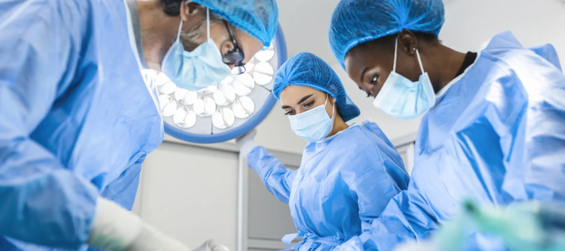 Surgical team in blue scrubs and masks performing operation under bright operating room lights.