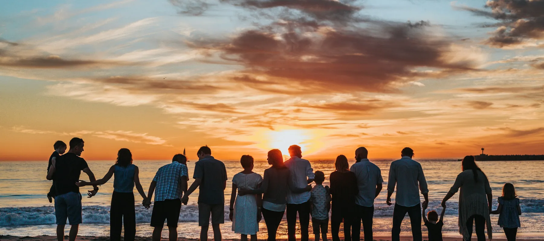 a group of people standing on a beach looking at the sunset