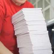 A printing plant worker holding a large stack of Perfect Bound books