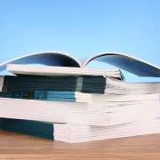A stack of miscellaneous booklets on a wooden surface against a blue background