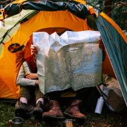 Two campers sitting in front of a tent surveying a large printed map