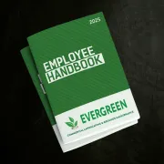 Two small employee handbooks lying in a stack on a dark surface