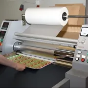 A commercial laminator applying plastic film to a printed substrate