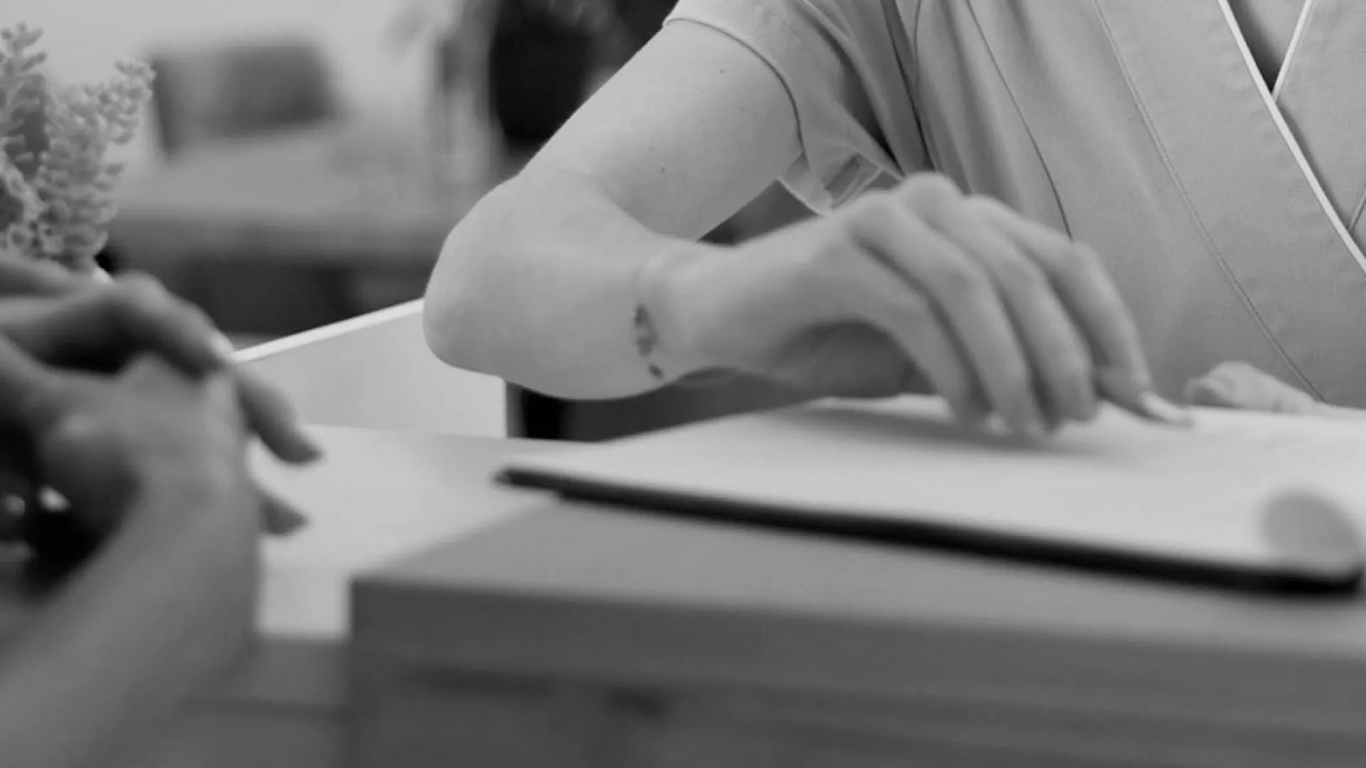 Healthcare professional writing notes at a clinic reception desk during patient consultation.