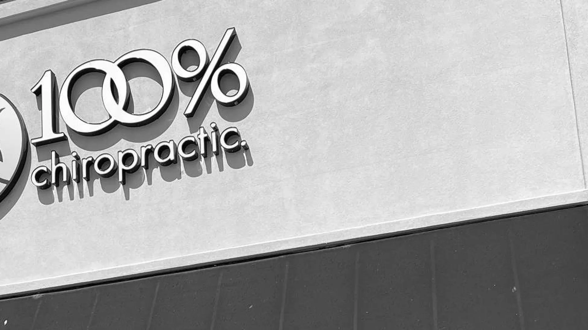 100% chiropractic logo with a sun and mountain icon on a building exterior wall in black and white