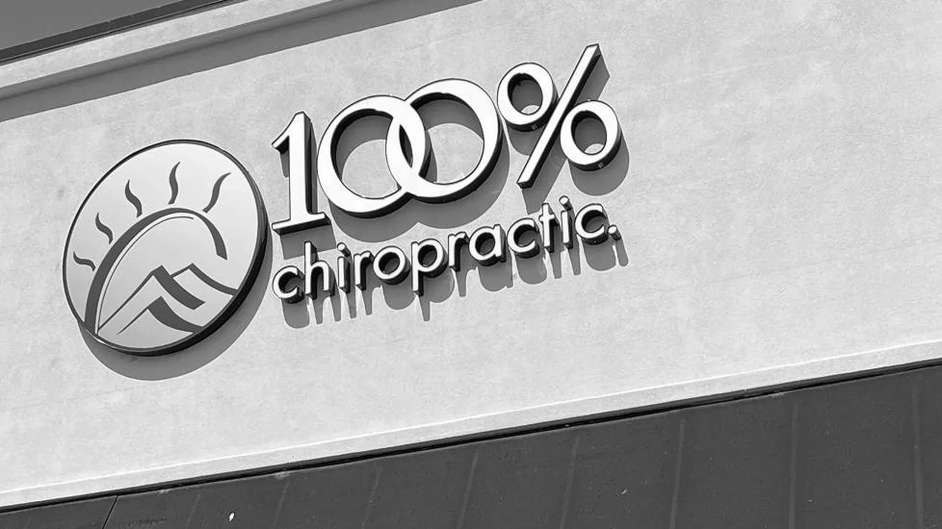 100% chiropractic logo with a sun and mountain icon on a building exterior wall in black and white