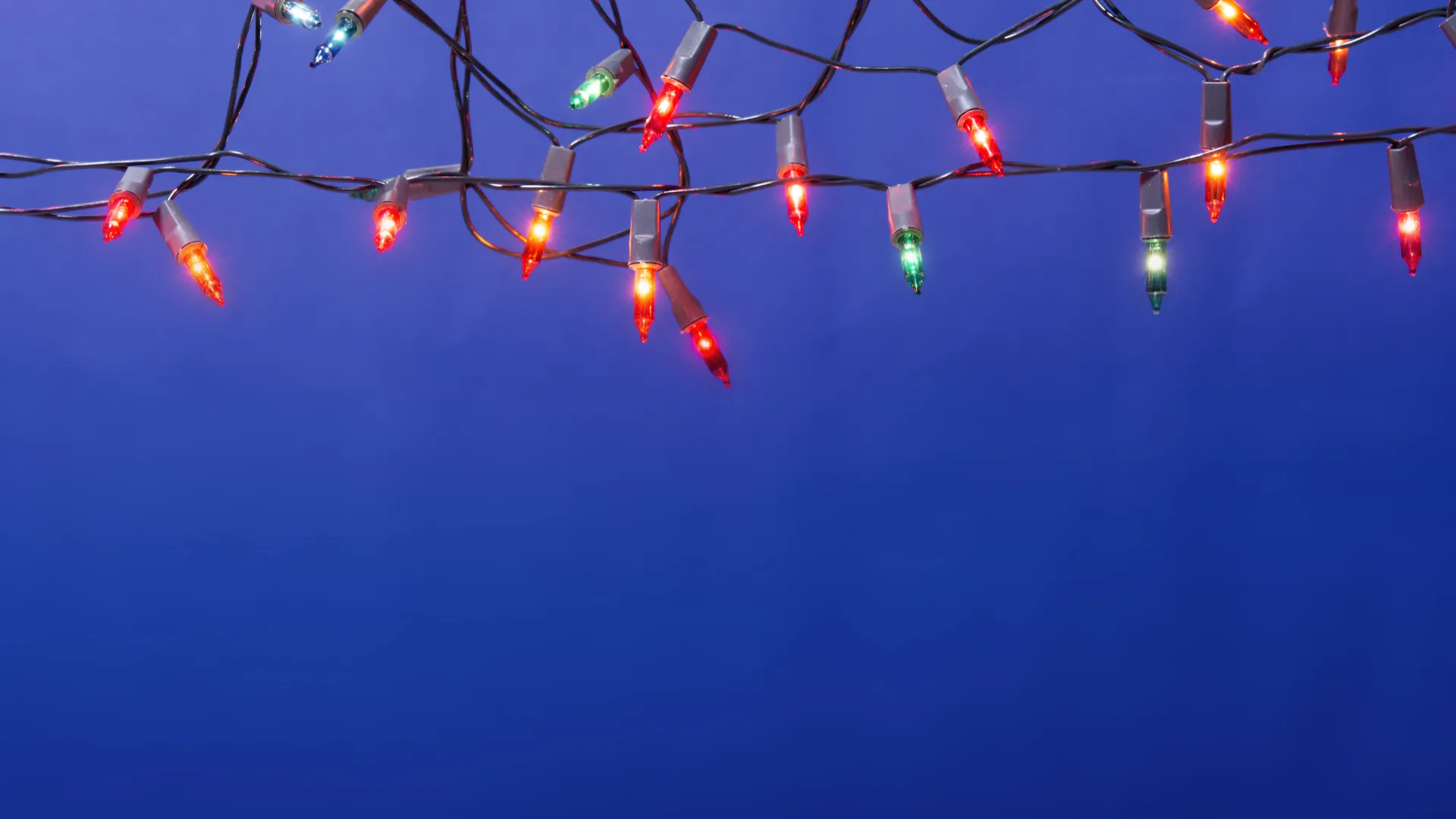 Colorful Christmas string lights glowing against a deep blue evening sky background.