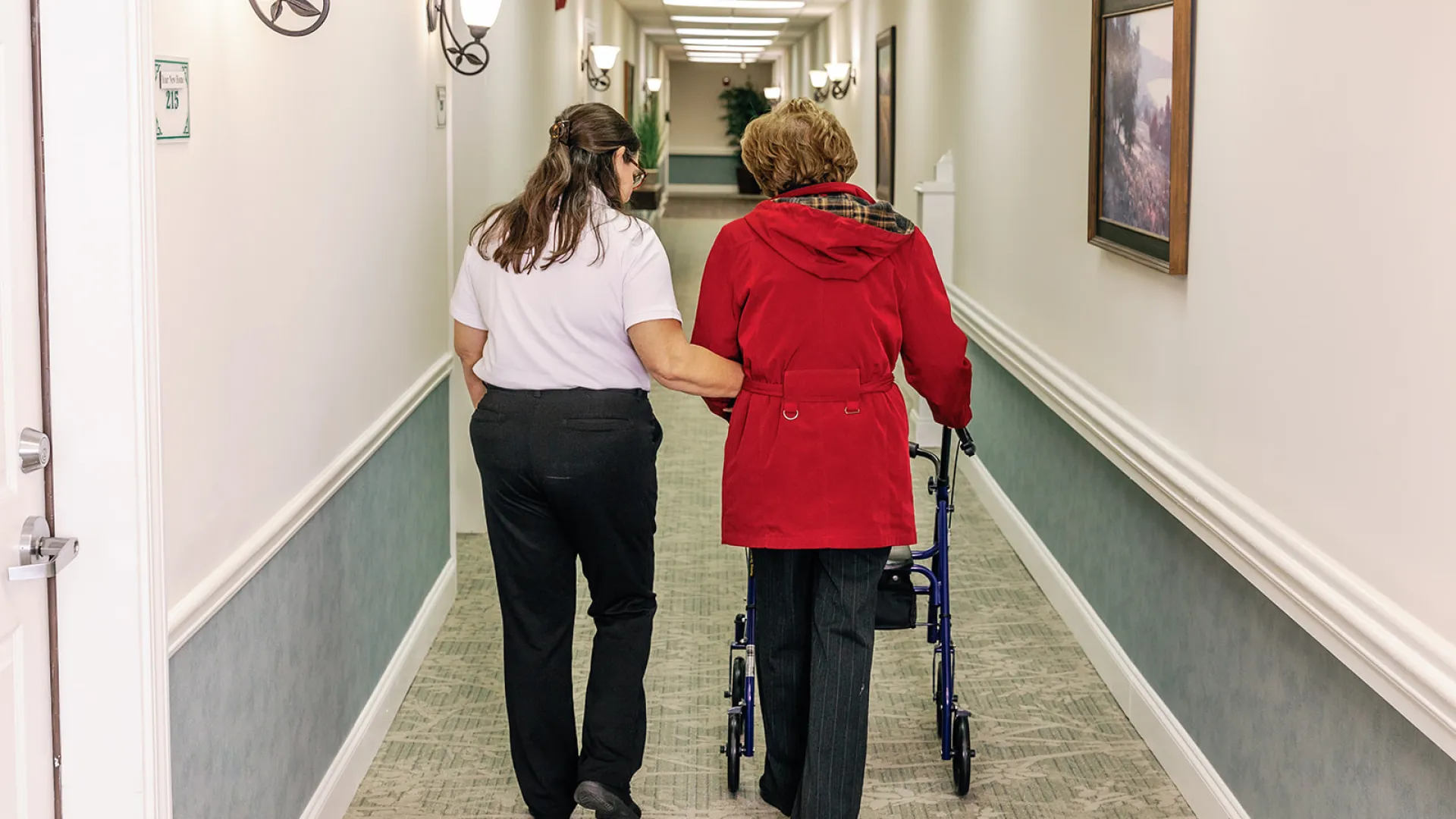 atlanta Home health Caregiver assisting elderly woman using a walker in a well-lit hallway of a care facility or home.