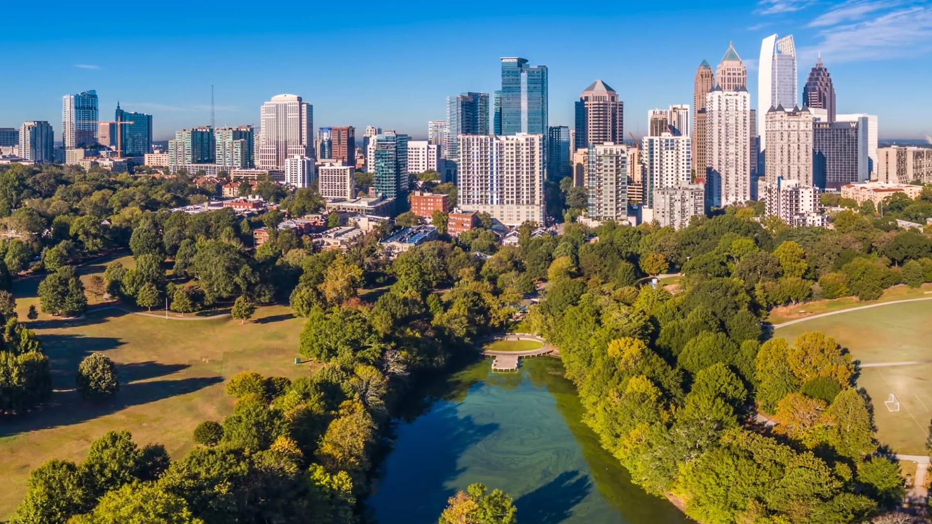 Aerial view of a city skyline with green parkland and a river running through the foreground on a clear day