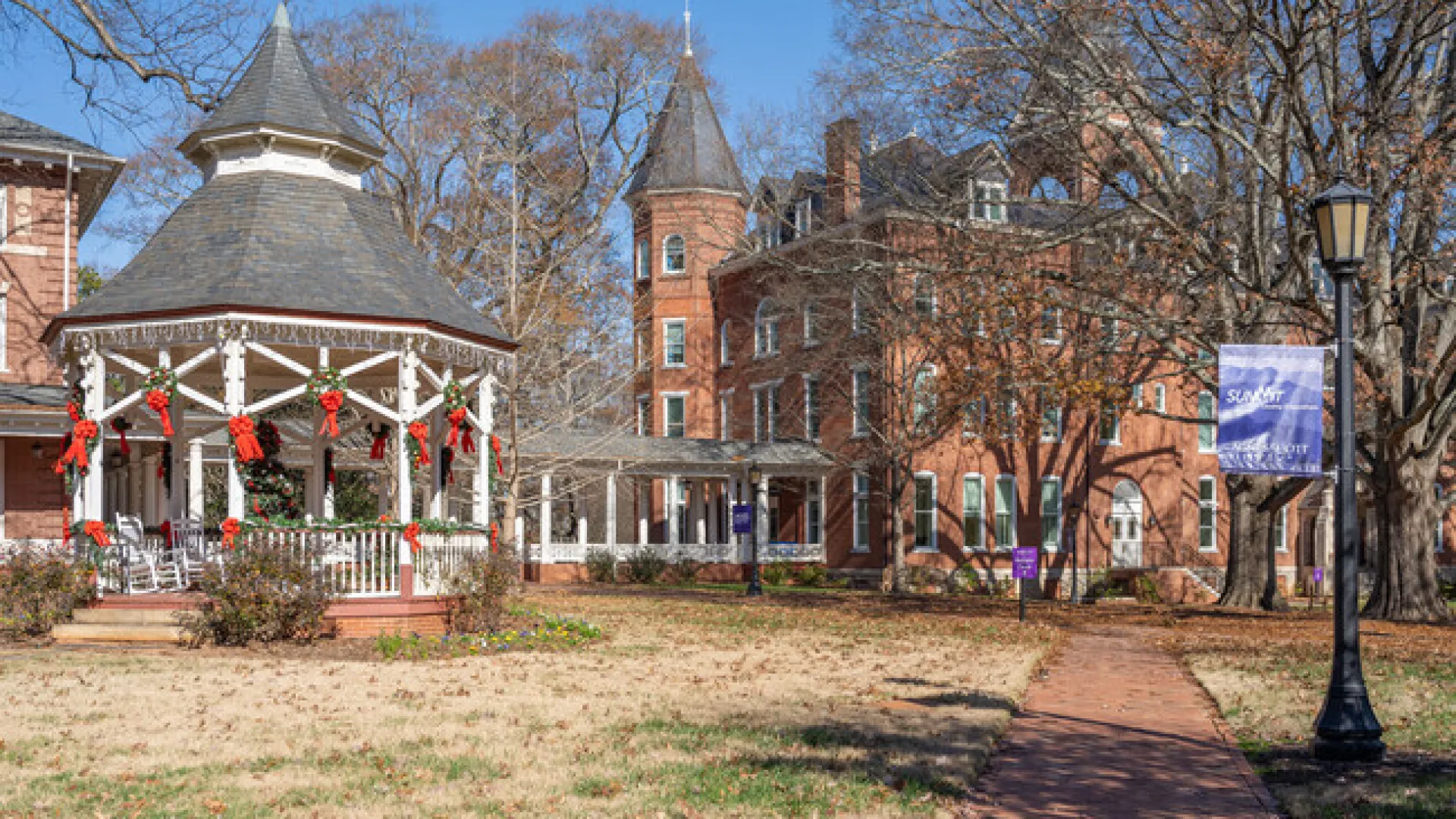 Charming gazebo adorned with holiday decor in a picturesque park setting, surrounded by historic buildings.