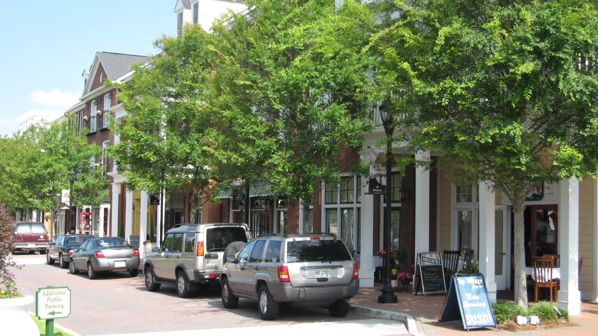 Street view of Smyrna with parked cars, brick sidewalks, green trees, and storefronts on a sunny day