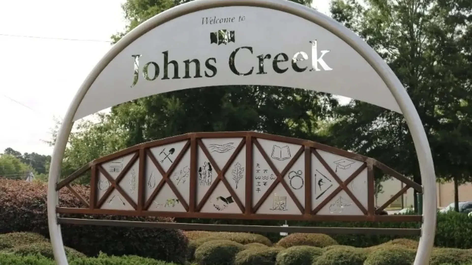 Welcome to Johns Creek metal sign with local symbols in green landscaped park area under trees