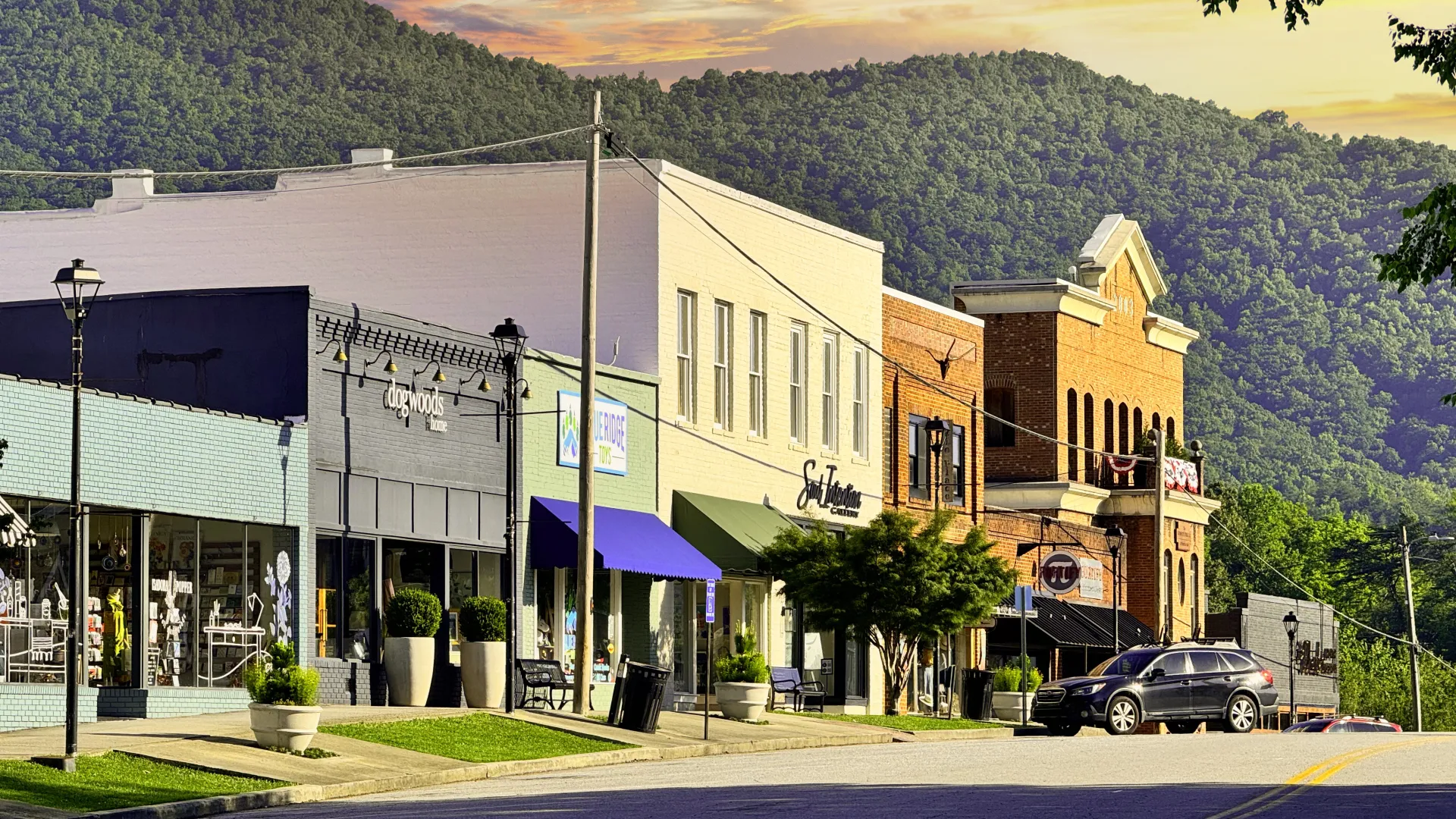 Charming small-town street with shops and mountains in the background during sunset.