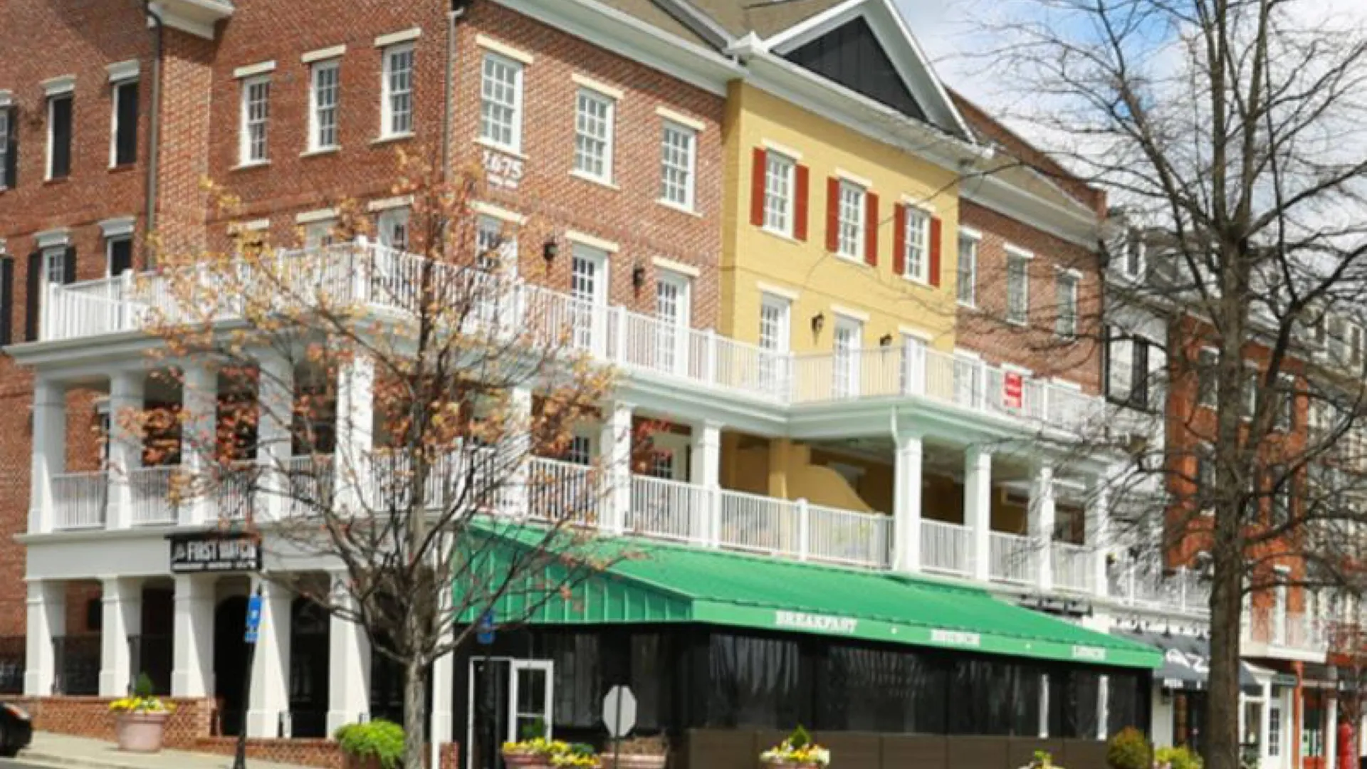 Three-story brick and yellow buildings in Smyrna with white balconies and green awning above a street corner cafe.